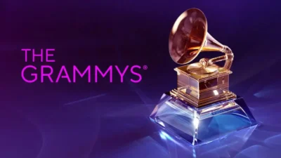 Zlatá gramofonová soška na průhledném podstavci, symbol cen Grammy, na fialovo-modrém pozadí s textem 'The Grammys'